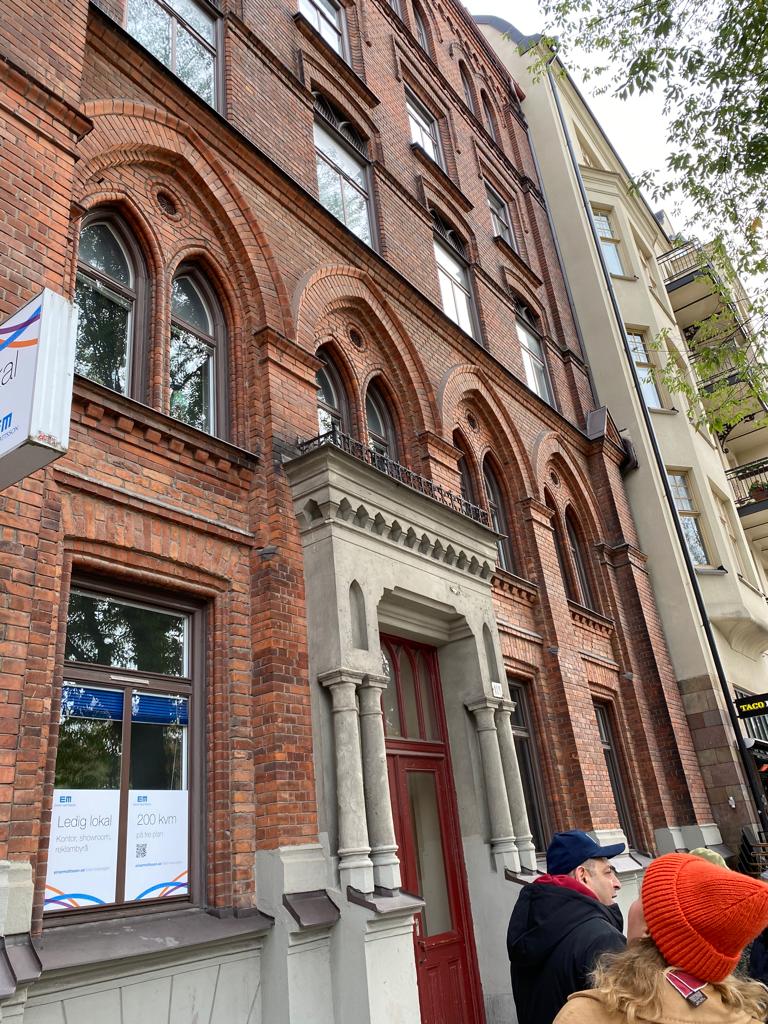 signpost with directions to museums in Spain, arrows on horizontal gray boards, grey pole, cityscape background.
